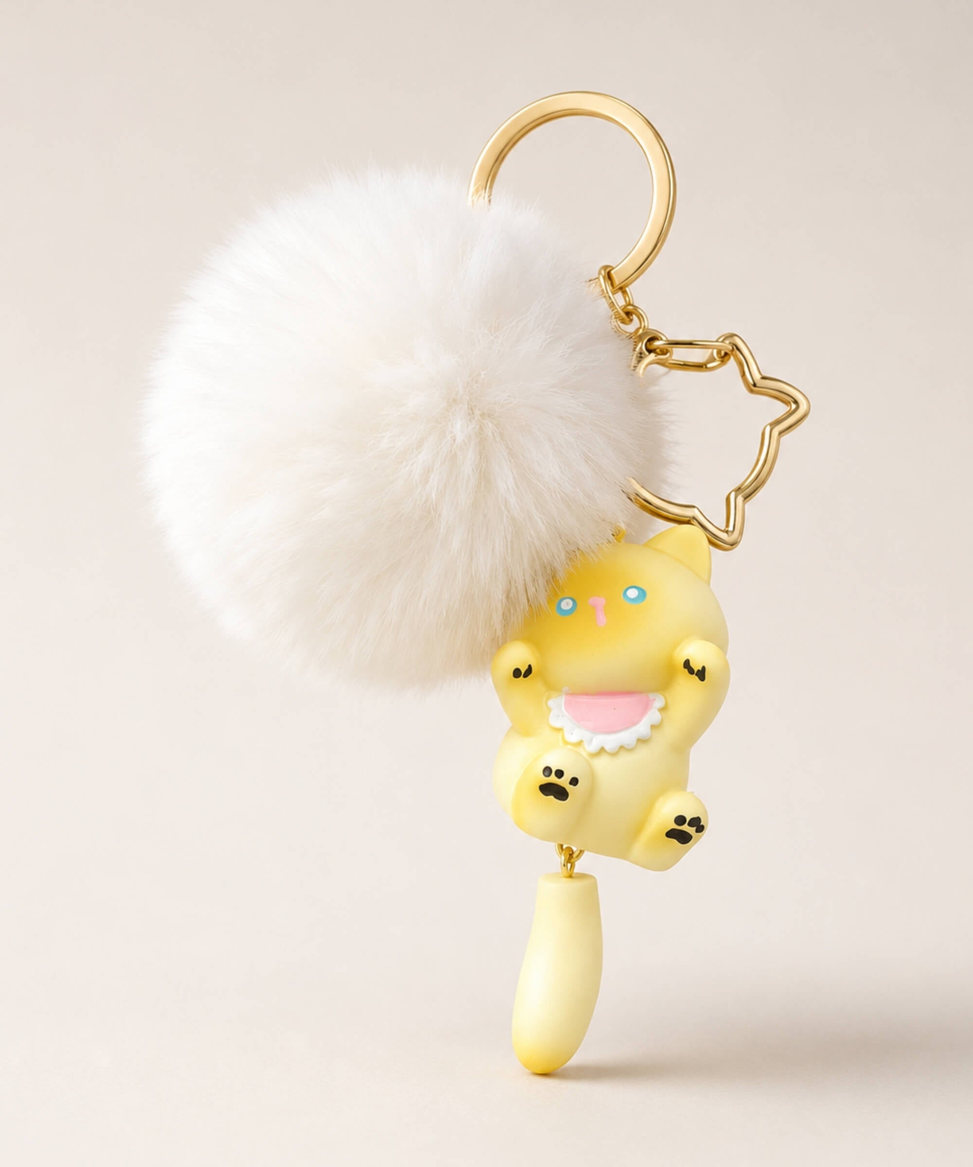Yellow cat pom pom resin keychain with white fluffy plush ball and gold hardware on a neutral background
